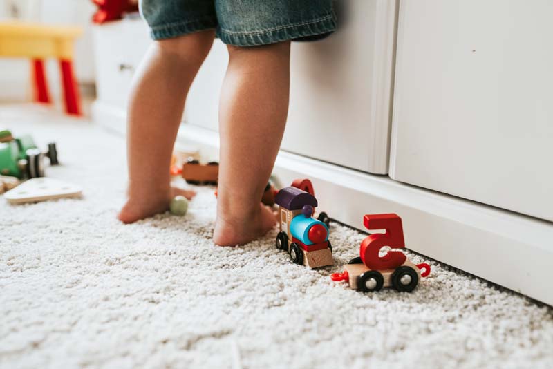 A baby is standing on the wall-to-wall carpet